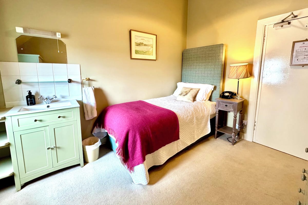 Une chambre à coucher comprenant un lit, une table de chevet, une lampe, ainsi qu’une salle de bain avec un lavabo et un miroir.