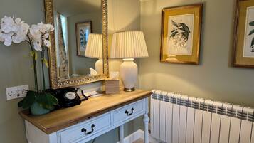 A bathroom with a vanity, a mirror, a lamp, a radiator, and framed botanical prints on the wall.