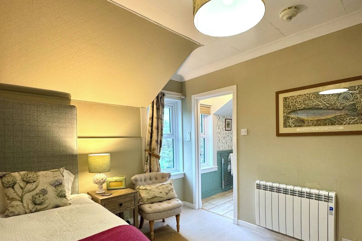 Une chambre à coucher avec un lit, une chaise, une lampe, un radiateur et un tableau encadré au mur.