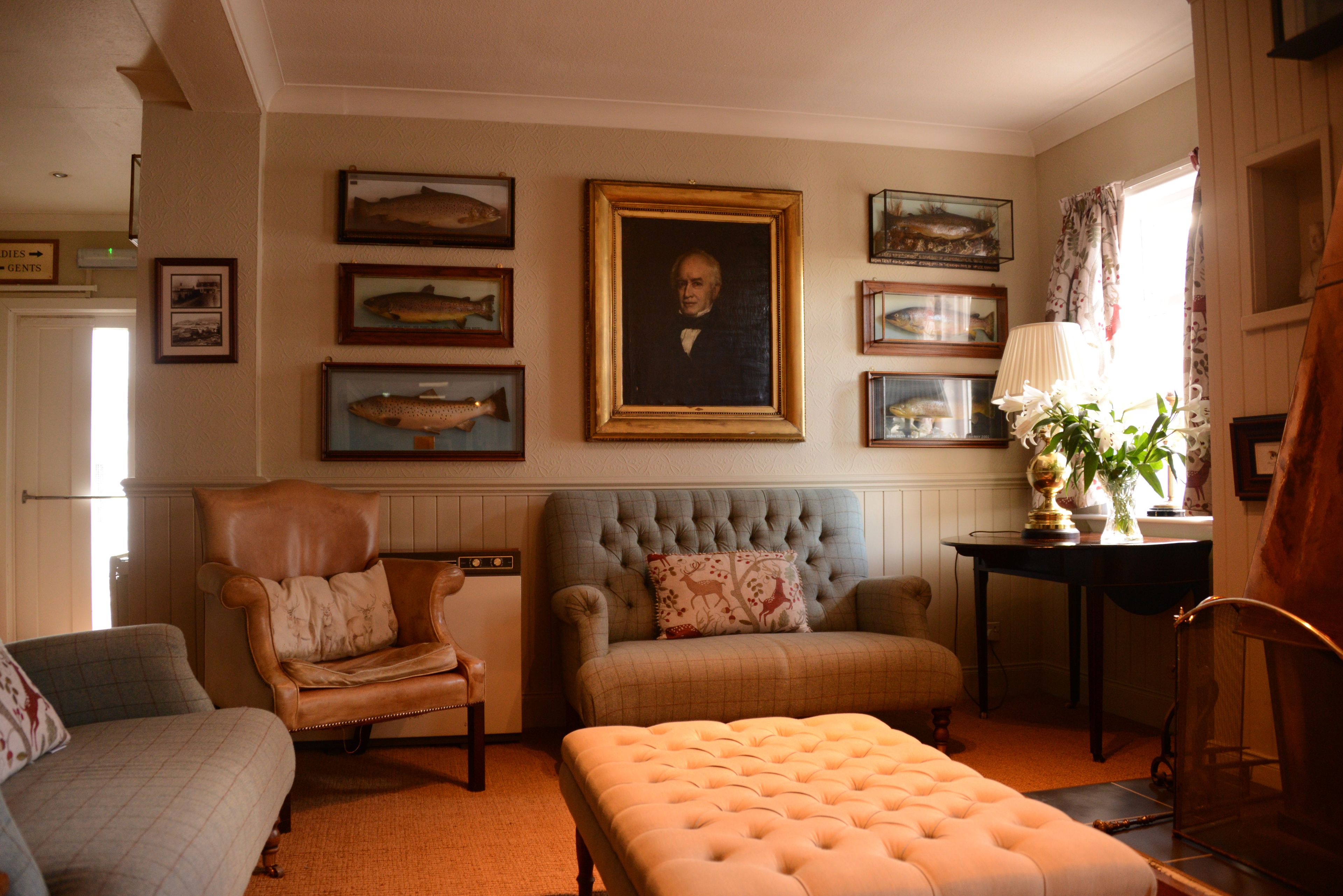 A living room with a sofa, armchair, and ottoman, a fireplace, and framed fish pictures on the wall.
