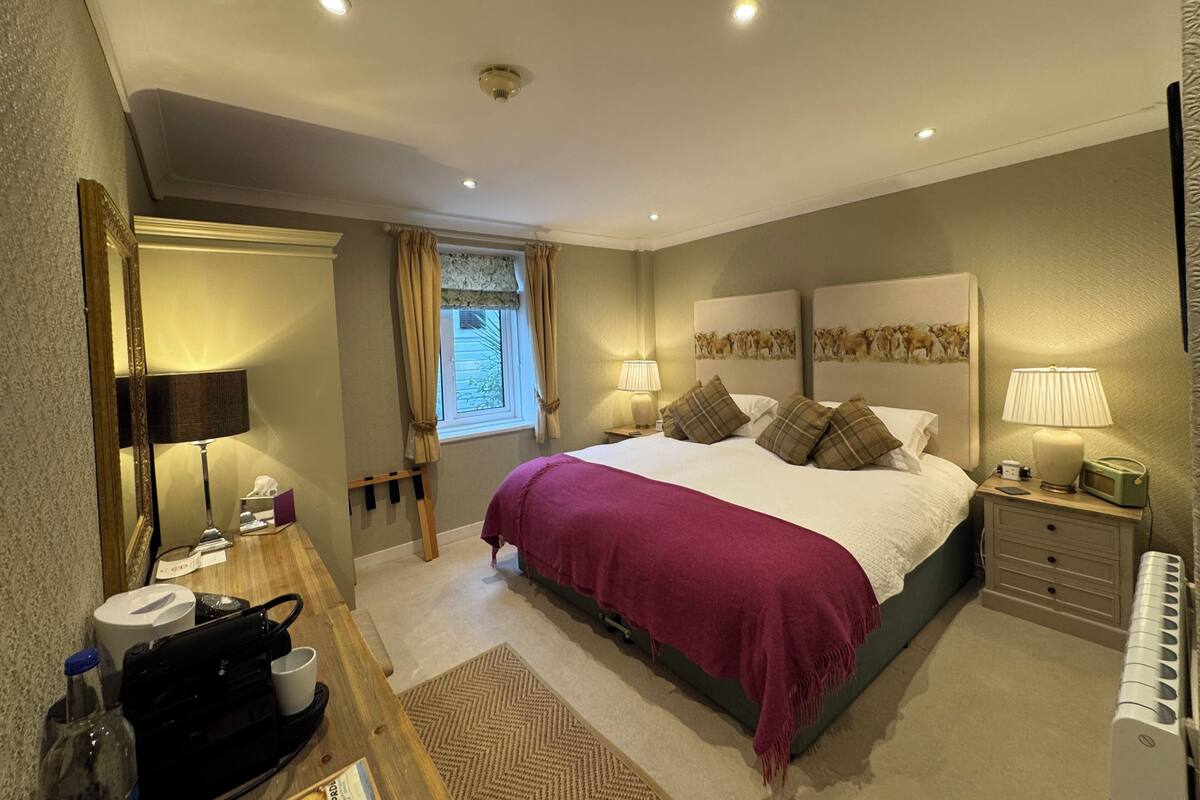 Une chambre à coucher comprenant un lit, des tables de chevet, un miroir, une fenêtre avec des rideaux et un radiateur.