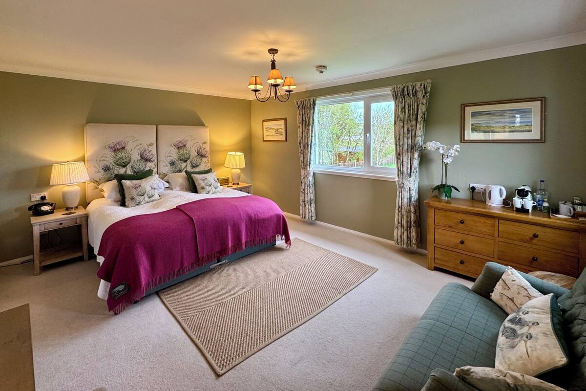 Une chambre à coucher comprenant un lit, des tables de chevet, une commode, une chaise, une fenêtre avec des rideaux et un lustre.