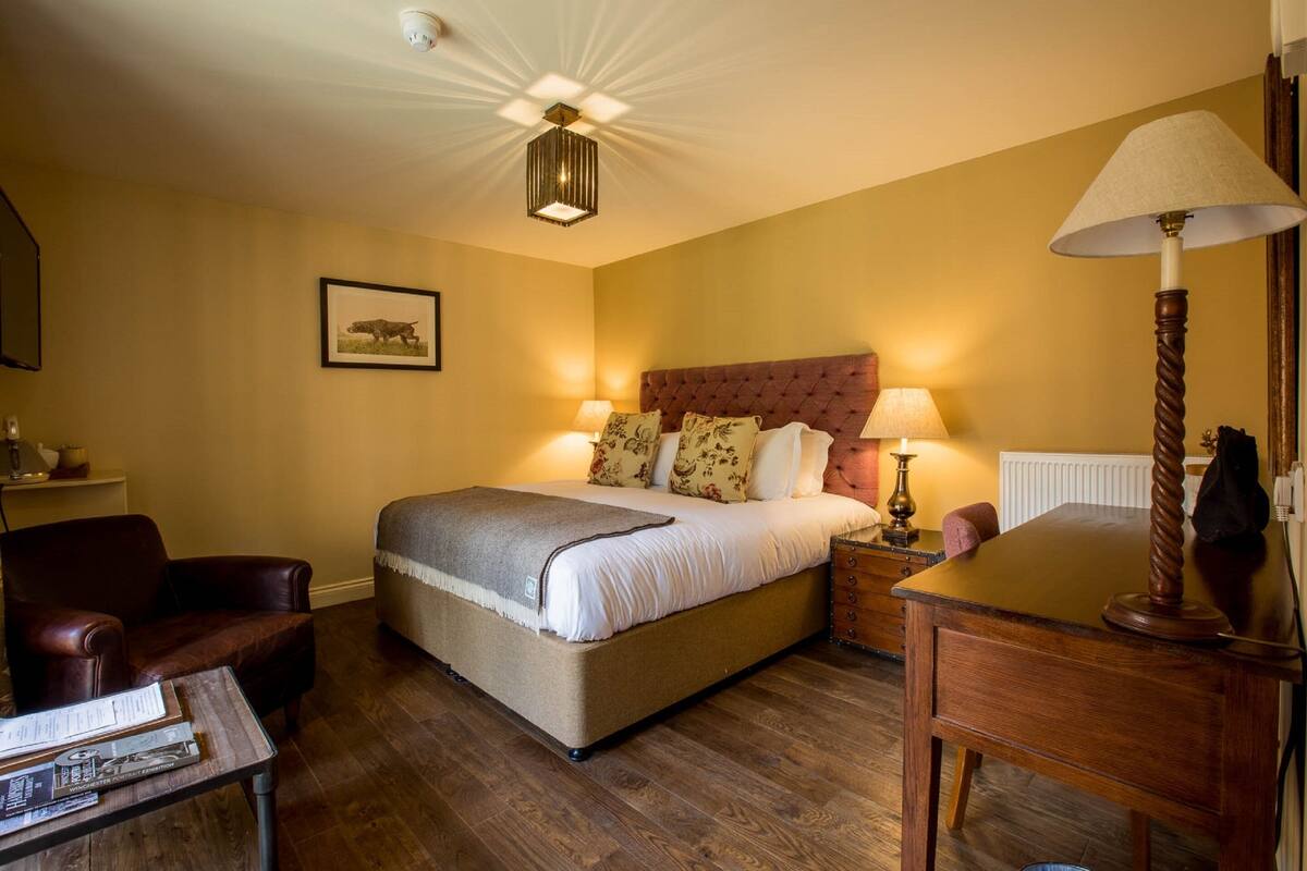 A bedroom with a large bed, a wooden nightstand, a chair, a desk, and a lamp.