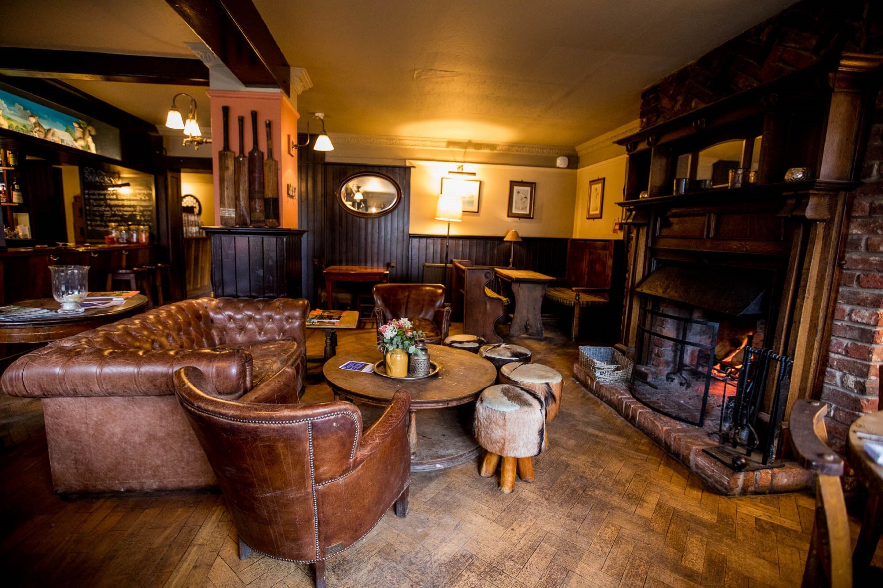 A cozy pub with leather furniture, a round table with a vase, and a brick fireplace.