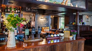 A bar area with a wooden counter, various bottles, a chalkboard menu, and a mural on the wall. - The Thomas Lord (Petersfield)