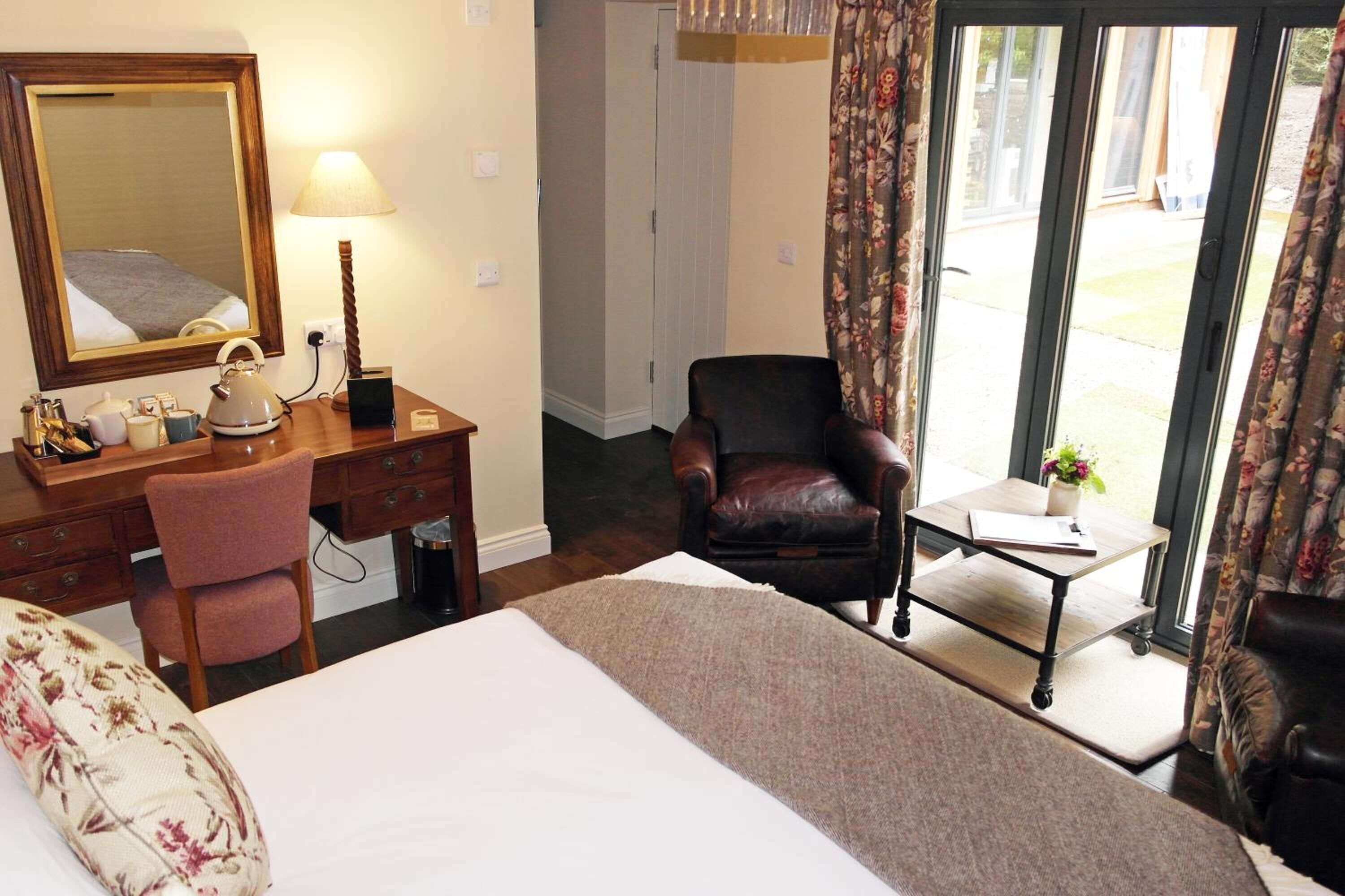 Habitación de hotel con cama, escritorio con silla, una mesita, espejo y vista a través de una puerta de cristal.