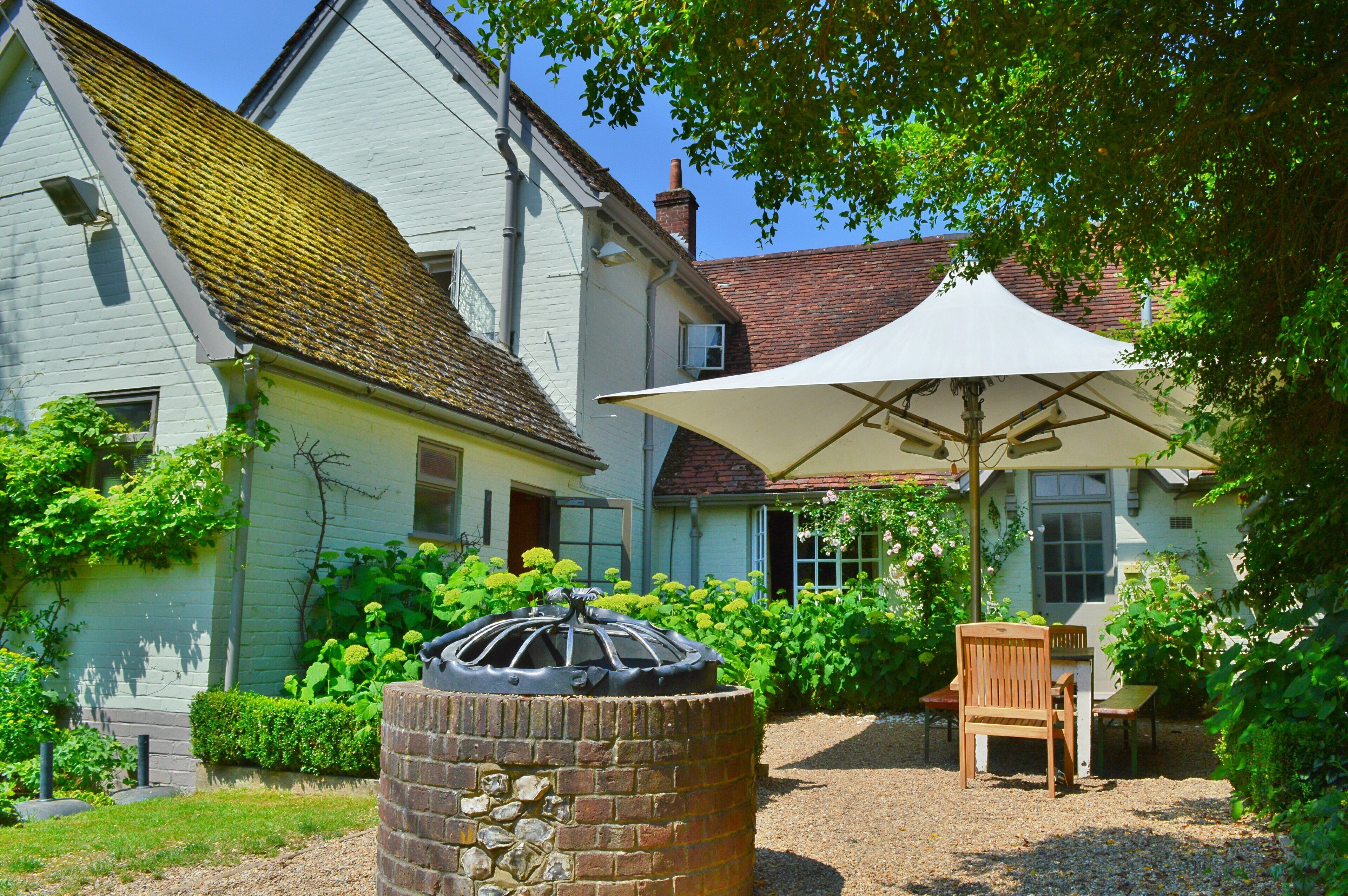 Een huis met een tuin, een terras met een tafel en stoelen, en een grote parasol.