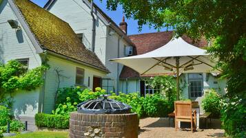 Een huis met een tuin, een terras met een tafel en stoelen, en een grote parasol.