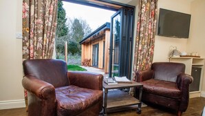 A living room with two leather armchairs, a coffee table, and a television on the wall. - The Thomas Lord (Petersfield)