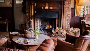 A cozy room with a fireplace, leather chairs, a round table with magazines, and a brick wall. - The Thomas Lord (Petersfield)