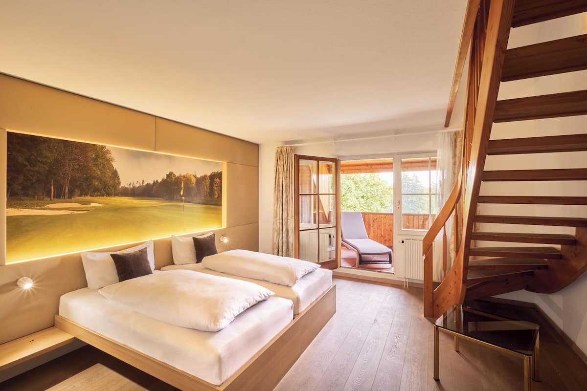 A modern hotel room with a large bed, a view of a golf course, and a wooden staircase.