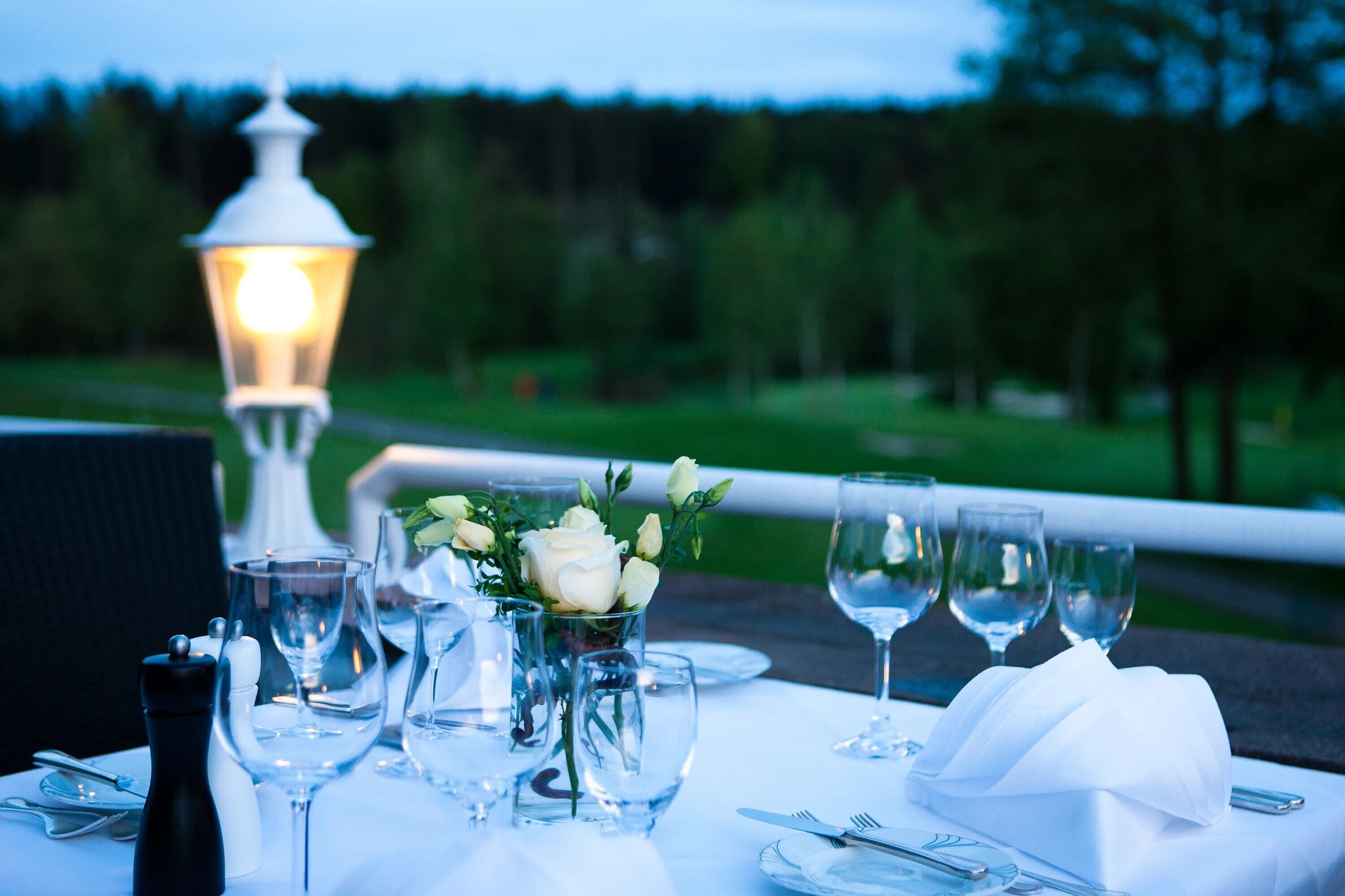 A table set for dining with a white tablecloth, clear glassware, and a lit lantern.
