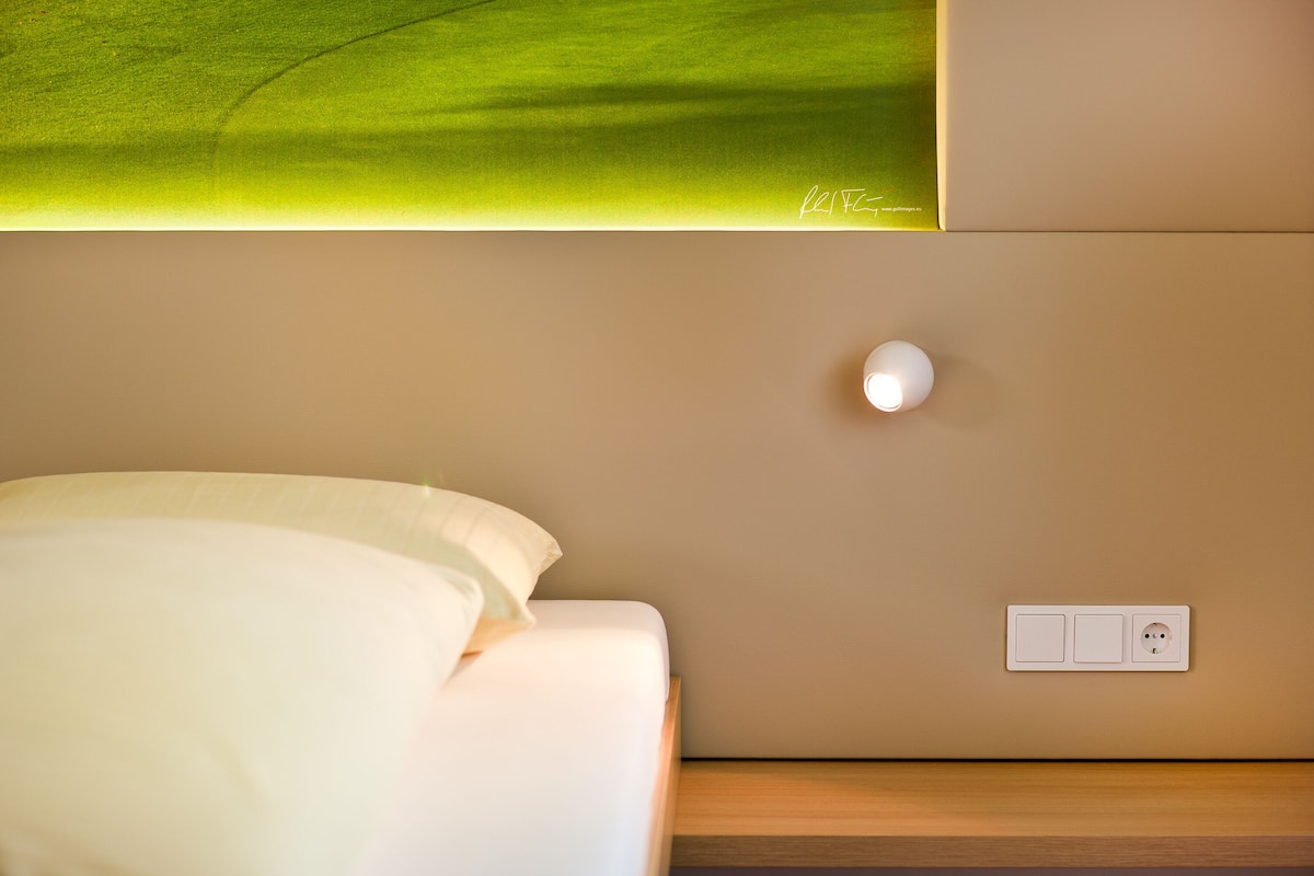 A neatly made bed with white linens, a bedside table, and a wall-mounted light fixture.