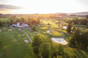 A large, white building with a red roof, surrounded by a well-maintained golf course with sand bunkers and a pond. - Golfhotel Bodensee by Michael Ritter (Weissensberg)