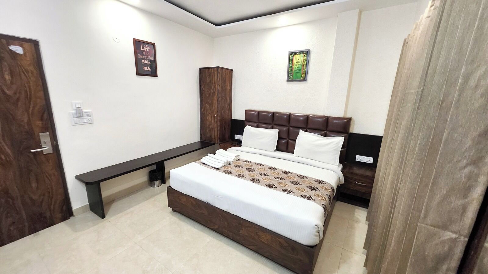 A bedroom with a bed, bedside tables, a bench, and two framed pictures on the wall.