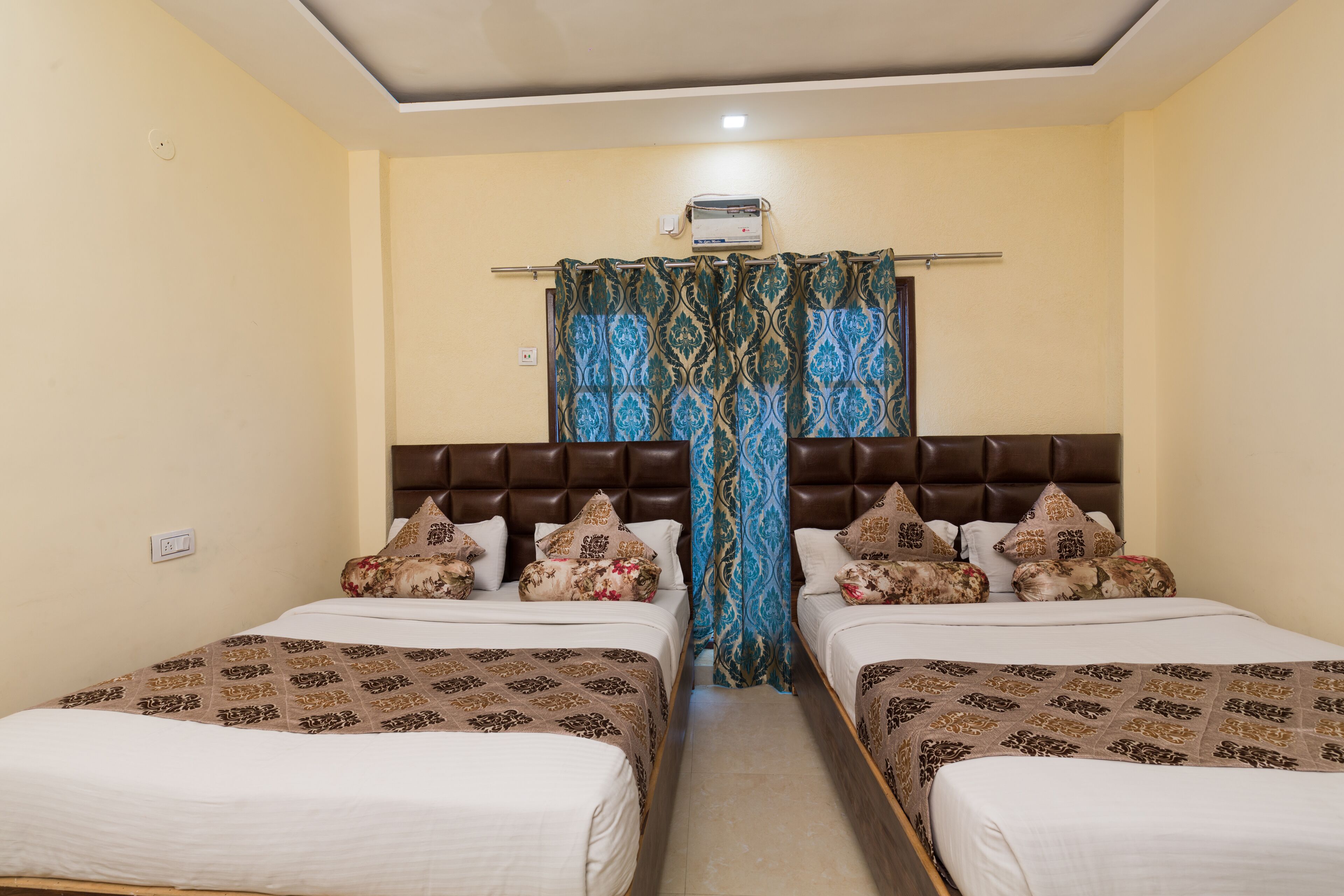 Une chambre d’hôtel avec deux lits, une tête de lit marron et un rideau à motifs bleus et dorés.