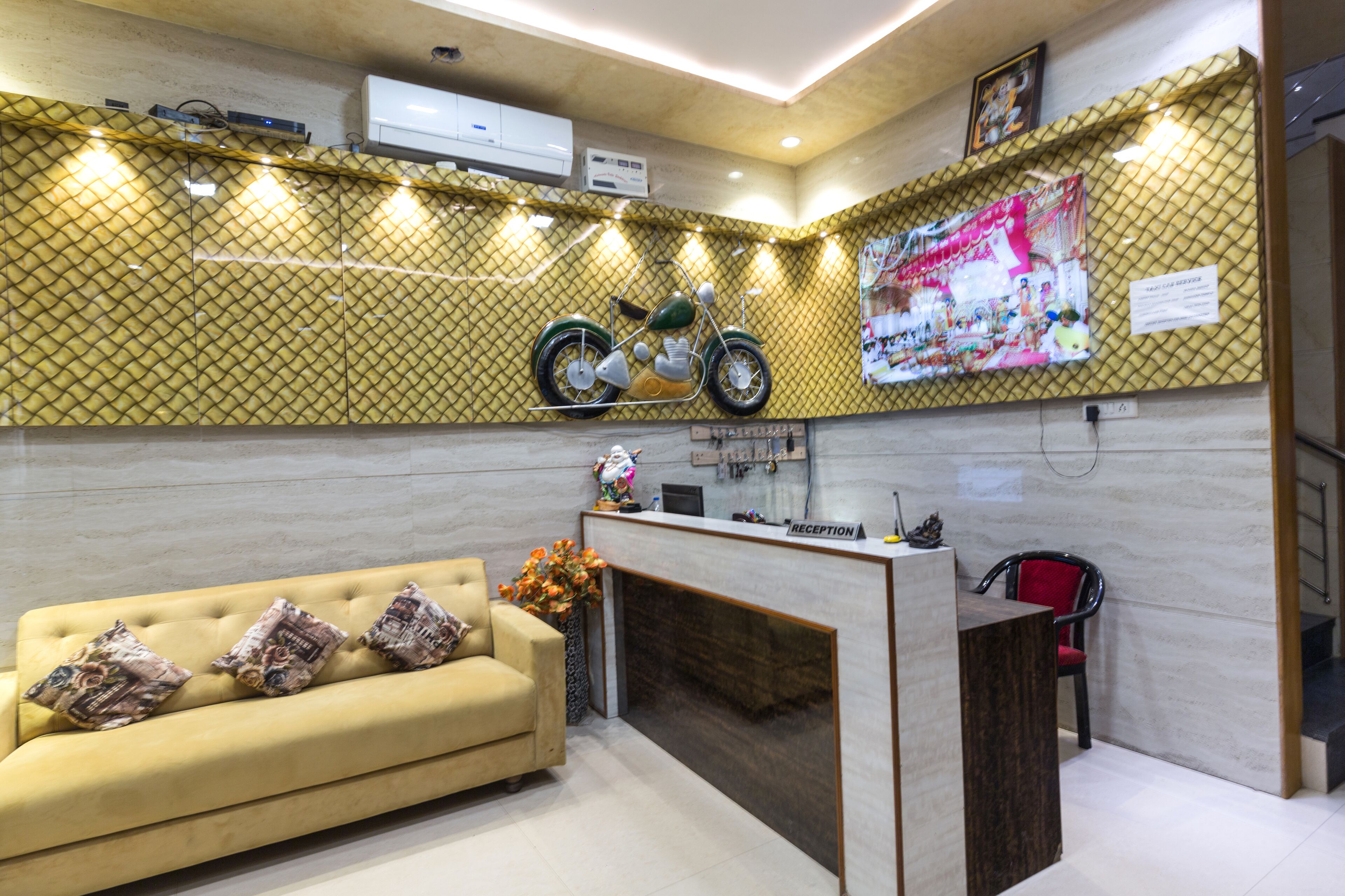 A reception area with a reception desk, a sofa with patterned cushions, a motorcycle decoration, and a wall-mounted television.