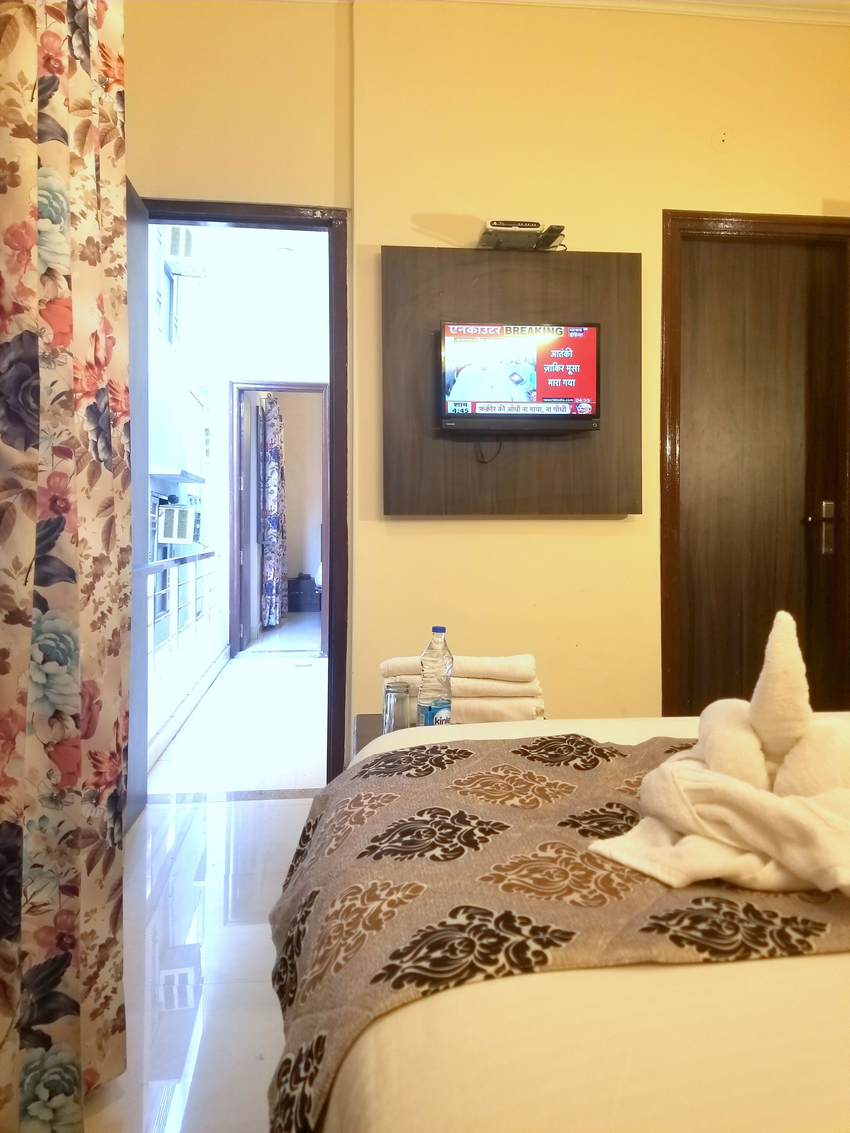 A hotel room with a bed, a television mounted on the wall, a bottle of water, and towels on the side table.
