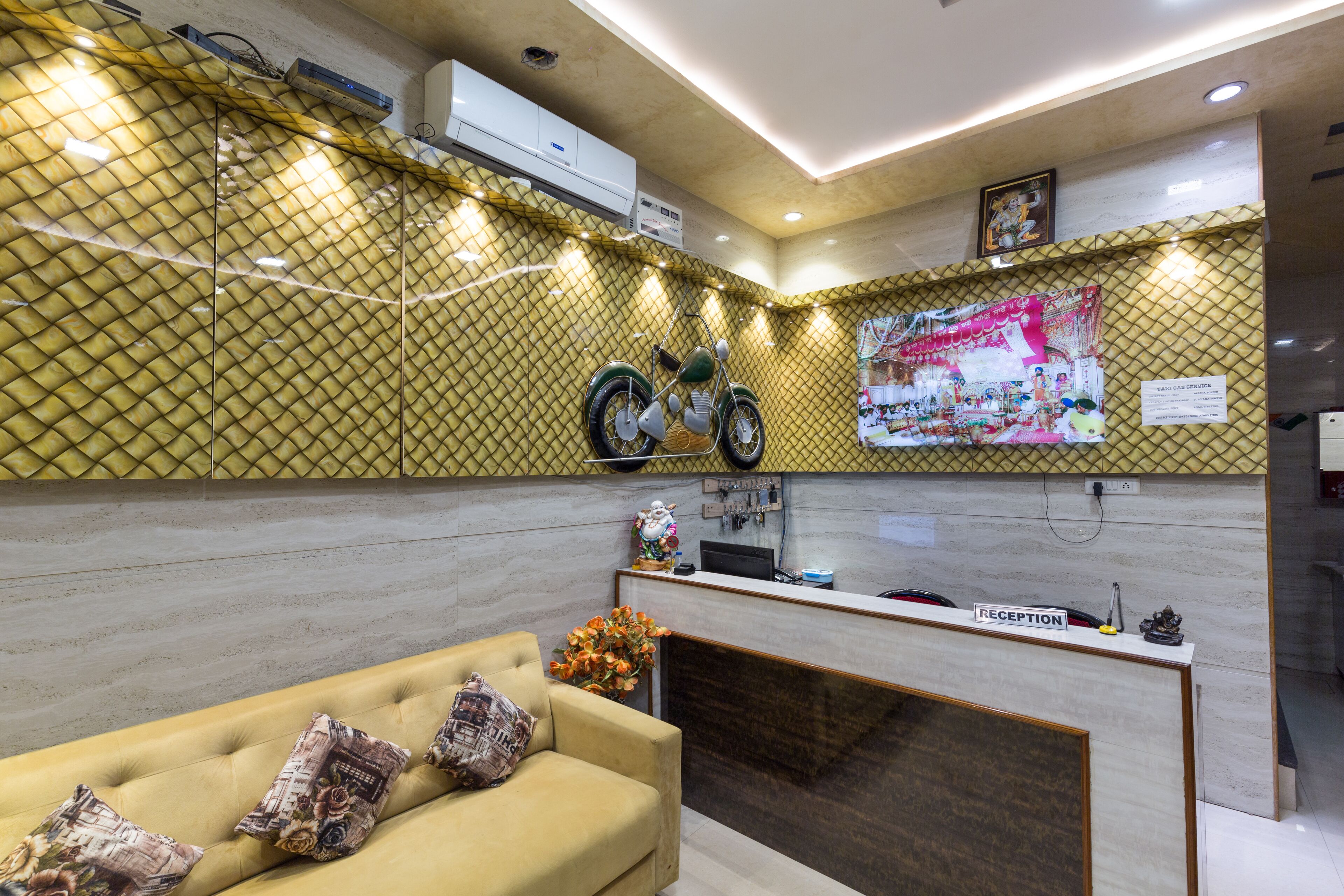 Un área de recepción con mostrador, un sofá con cojines estampados, una motocicleta decorativa y un aire acondicionado de pared.
