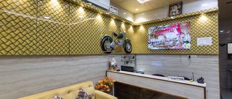 Un área de recepción con mostrador, un sofá con cojines estampados, una motocicleta decorativa y un aire acondicionado de pared.