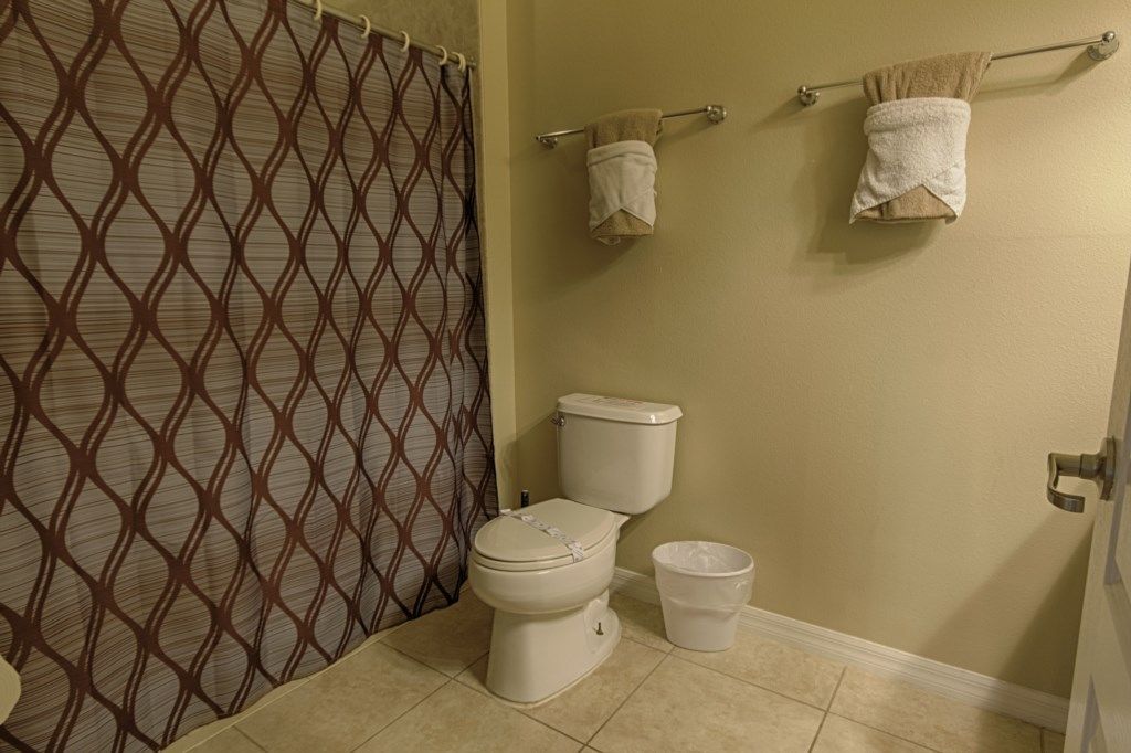Une salle de bain avec des toilettes, un rideau de douche et deux serviettes sur un porte-serviettes.