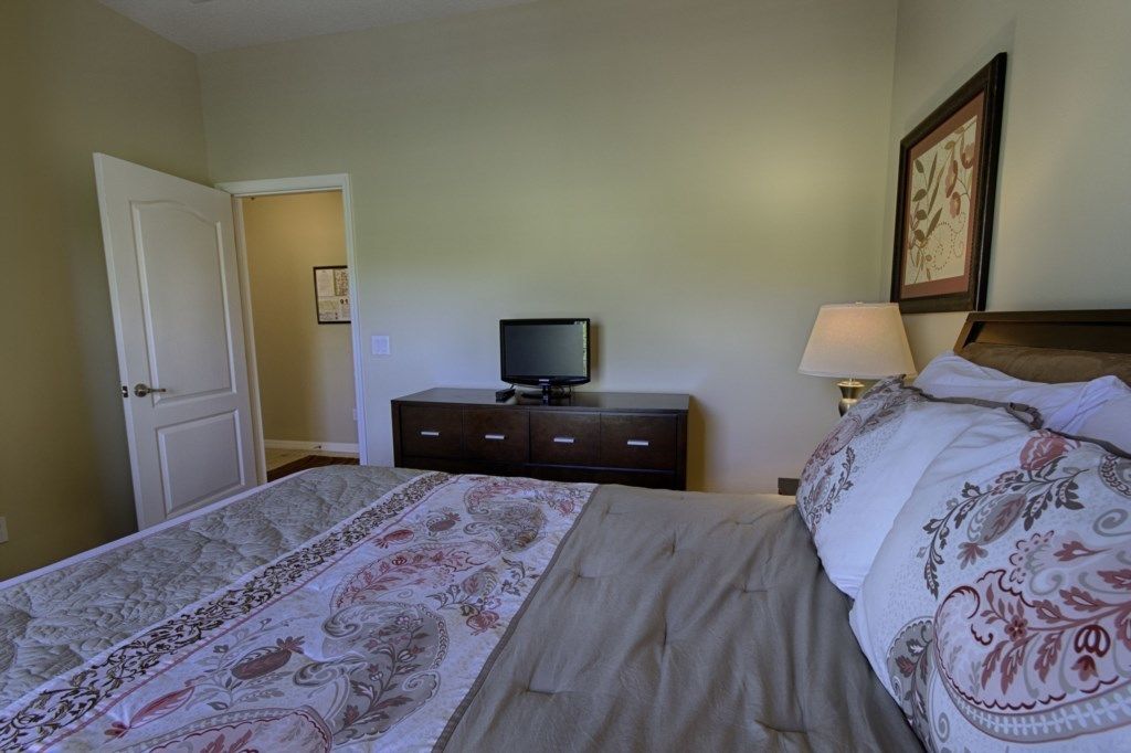 Un dormitorio con cama, cómoda, televisor y lámpara.