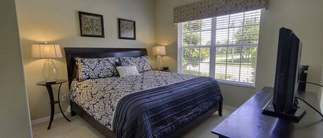 A bedroom with a bed, two bedside lamps, a TV, and a window with blinds.
