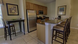 A kitchen with wooden cabinets, a stainless steel refrigerator, a microwave, a stove, and a dining area with chairs.