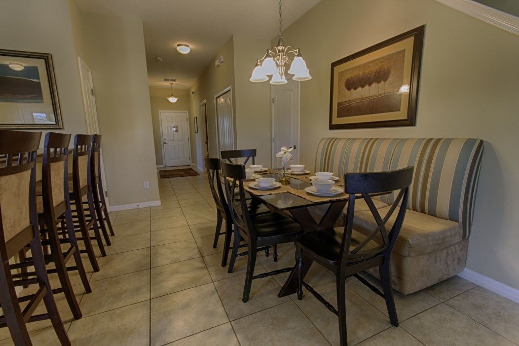 A dining area with a table set for four, surrounded by chairs, a cushioned bench, and a chandelier.