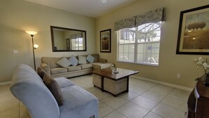 A living room with a sofa, a coffee table, a floor lamp, and a large window with blinds.