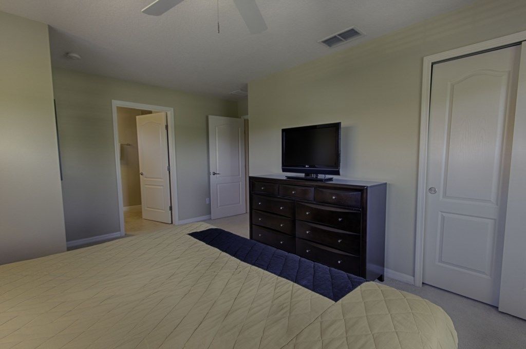A bedroom with a bed, a dresser, a television, and two doors.
