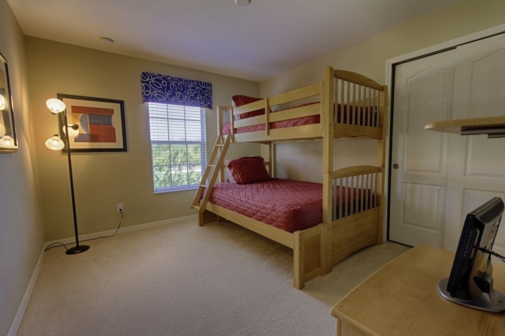 A room with a bunk bed, a desk with a computer, a lamp, and a window with blinds.