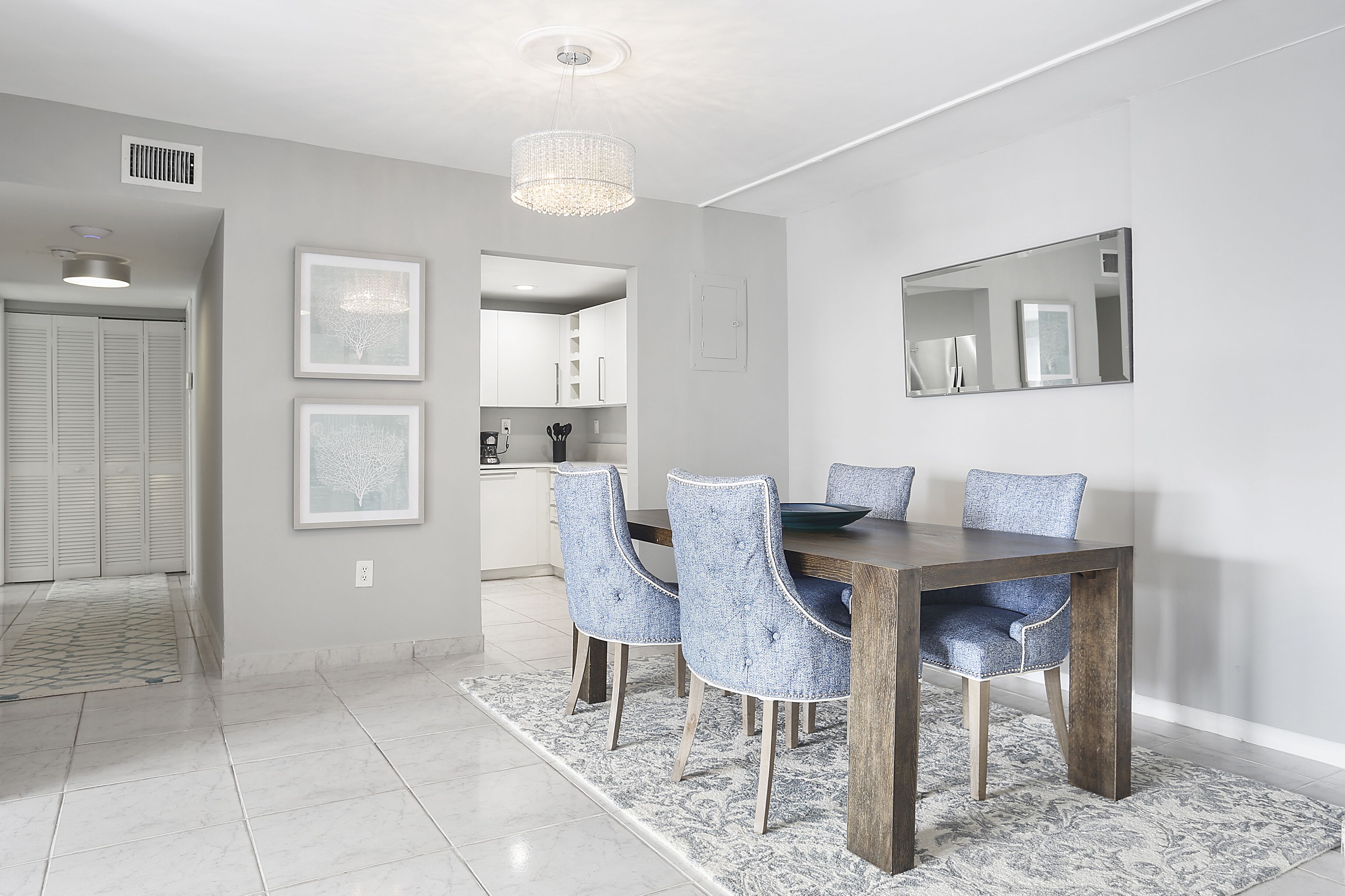 A dining area with a wooden table and four upholstered chairs, a chandelier, and framed artwork on the walls.