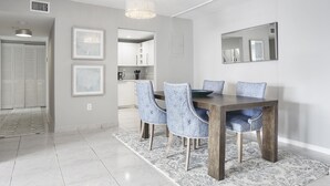 A dining area with a wooden table and four upholstered chairs, a chandelier, and framed artwork on the walls. - Modern 2BR/2BA Ocean View Beach Condo STR-09902 (Sunny Isles Beach)