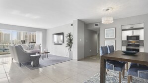 A modern living room with a dining area, large windows, and a view of the city. - Modern 2BR/2BA Ocean View Beach Condo STR-09902 (Sunny Isles Beach)