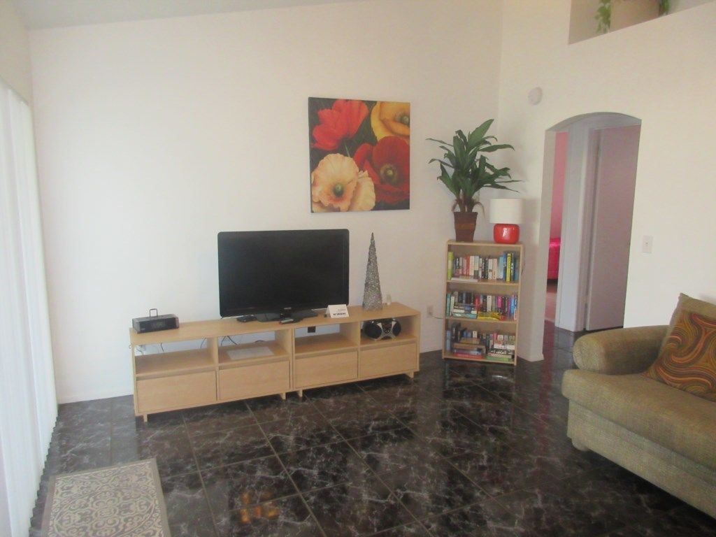 A living room with a flat-screen TV on a wooden stand, a bookshelf, a potted plant, a sofa, and a door.