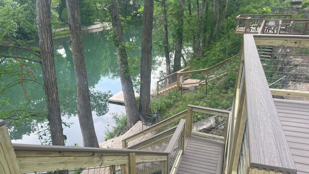 A wooden deck with railings overlooking a body of water surrounded by trees.