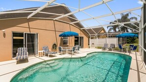 A pool area with lounge chairs and umbrellas, a covered patio, and a building with a beige exterior. - 4BR Pool Home Rolling Hills by SHV-7979 (Kissimmee)