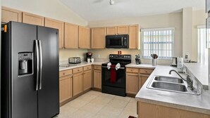 A modern kitchen with wooden cabinets, a stainless steel refrigerator, a microwave, a stove, and a sink. - 4BR Pool Home Rolling Hills by SHV-7979 (Kissimmee)