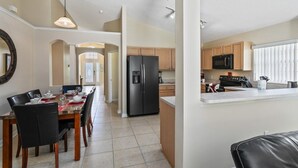 A modern kitchen with a central island, a dining area with a table set for four, and a view of the adjacent living area. - 4BR Pool Home Rolling Hills by SHV-7979 (Kissimmee)