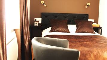 A hotel room with a bed, a nightstand, a chair, and a window with curtains.