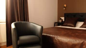 Una habitació d'hotel amb un llit gran, una cadira, una tauleta de nit i una làmpada penjada a la paret.