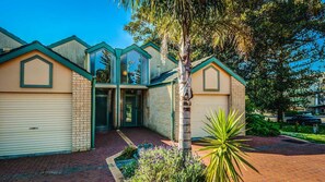 A two-story house with a garage, a front door, and a small garden with plants and a tree. - Findlay on the Bay - sleeps 8 (Cowes)