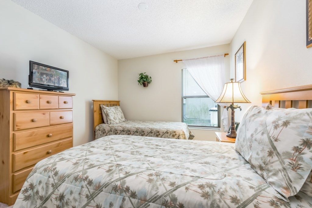 A bedroom with a bed, a dresser, a television, a window with curtains, and a lamp.