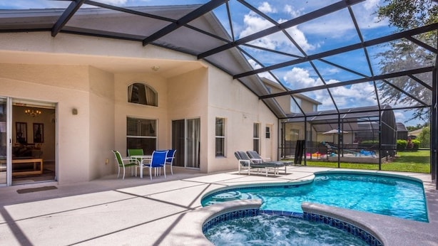 Ein überdachter Pool im Freien mit Liegestühlen und einem Whirlpool, umgeben von einem Haus mit Terrasse und überdachter Eingangshalle.