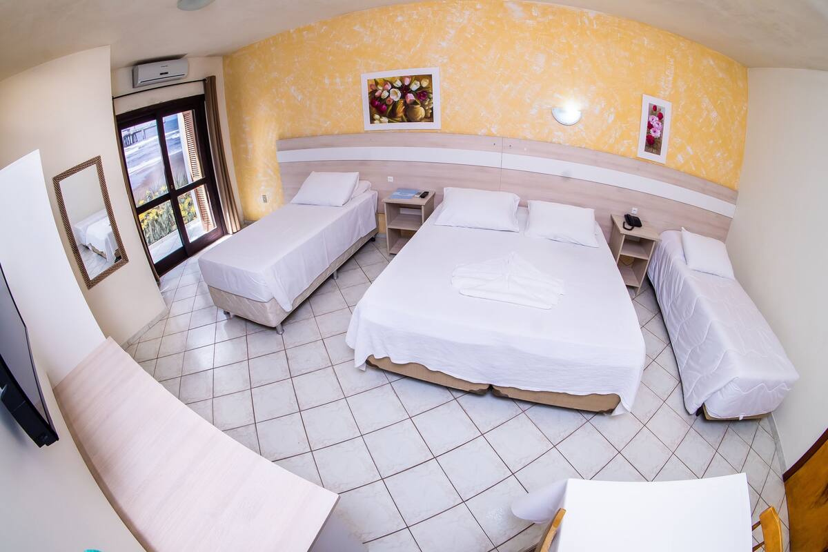 A hotel room with a curved wall, two single beds, a double bed, a sofa, a small table, and a TV.