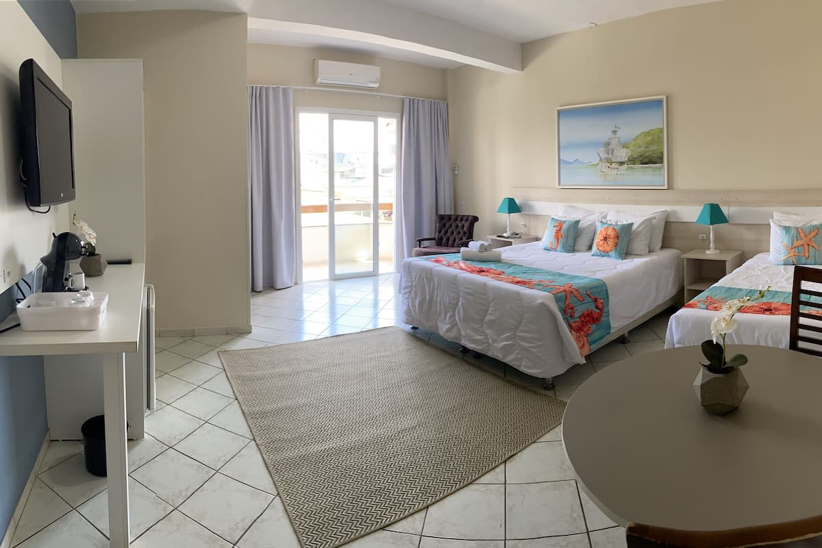 A hotel room with a bed, bedside tables, a desk, a chair, a table, and a painting on the wall.