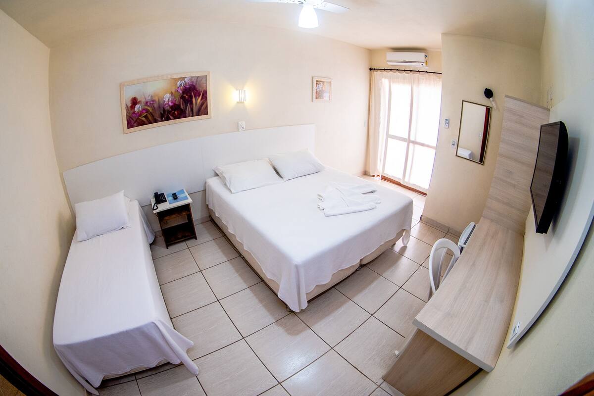 A hotel room with two single beds, a small bedside table, a mirror, a TV, and a window with curtains.