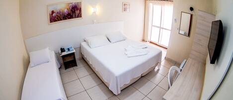 Habitación de hotel con dos camas individuales, una mesita de noche, un espejo, televisor y ventana con cortinas.