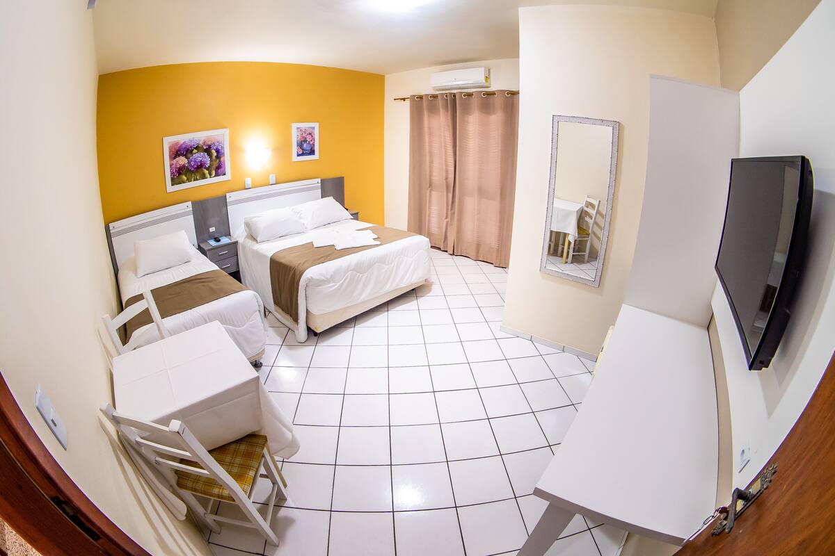 A hotel room with a bed, two bedside tables, a desk, a chair, a TV, and a window with curtains.